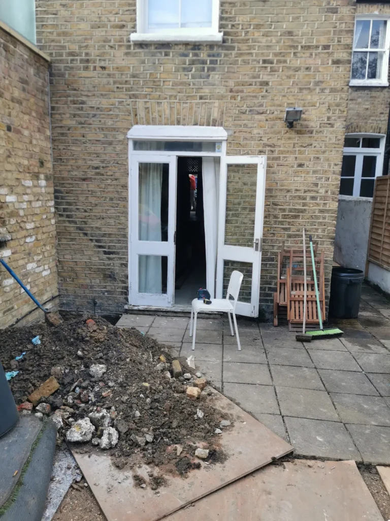 Existing rear elevation of Chiswick home with visible trial pit for foundation investigation