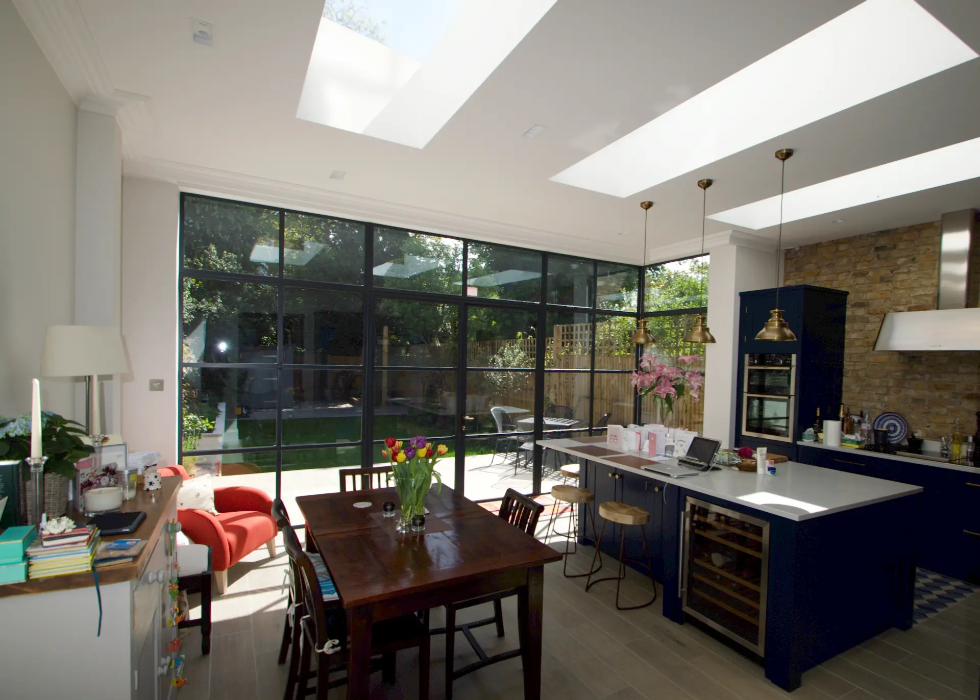 Bright Ealing ground floor extension with a modern kitchen featuring blue units, skylights, and a Crittall door overlooking a garden