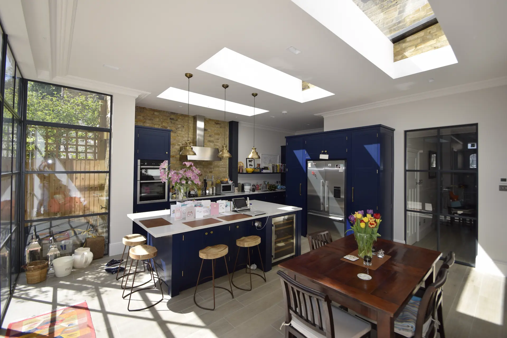 Open-plan kitchen in an Ealing ground floor extension with blue units, skylights, and a Crittall sliding door leading to the hall